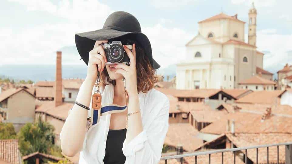 gadis cantik pakai topi sedang menggunakan kamera untuk foto pemandangan desa
